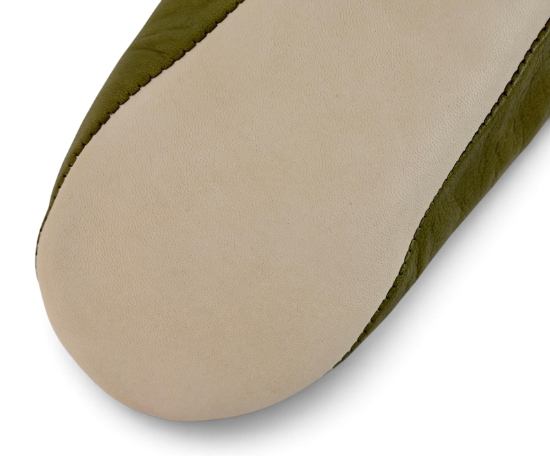 May include: A close-up view of the sole of a shoe, featuring a smooth, light beige leather bottom panel stitched to an olive green leather upper section. The stitching is visible along the seam where the two distinct leather pieces meet.