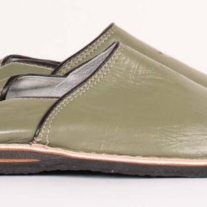 May include: A pair of olive green leather slippers featuring a smooth finish, black trim along the collar, and a layered sole consisting of a thin light-colored middle layer sandwiched between a dark brown upper layer and a black textured base.