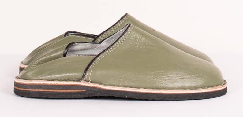 May include: A pair of olive green leather slippers featuring a smooth finish, black trim along the collar, and a layered sole consisting of a thin light-colored middle layer sandwiched between a dark brown upper layer and a black textured base.