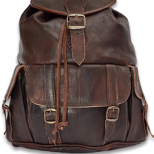 May include: Dark brown leather backpack with multiple buckles and straps.  The backpack has a large main compartment and a smaller front pocket.  Dark Brown Large.