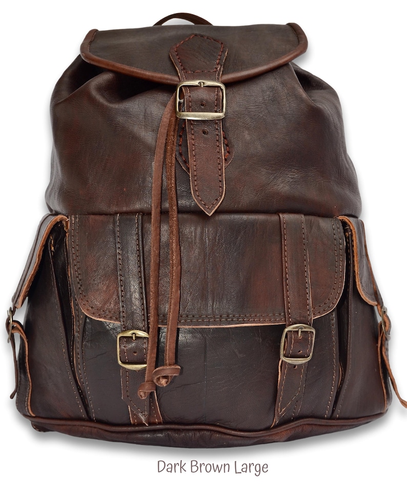 May include: Dark brown leather backpack with multiple buckles and straps.  The backpack has a large main compartment and a smaller front pocket.  Dark Brown Large.
