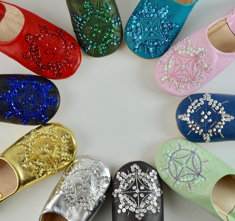 Puede incluir: Un conjunto de diez zapatillas de cuero de colores con adornos de joyas en forma de copo de nieve. Las zapatillas est&aacute;n dispuestas en c&iacute;rculo sobre un fondo blanco.