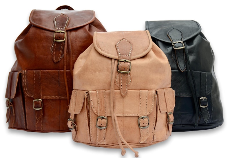 May include: Three leather backpacks in brown, tan, and black. Each backpack has a drawstring closure, a flap with a buckle, and multiple pockets.