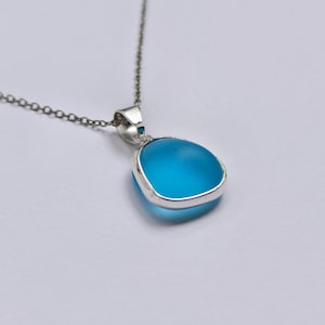 Pu&ograve; includere: Collana d'argento con un ciondolo a forma di pietra triangolare arrotondata blu chiaro. La pietra &egrave; incastonata in una lunetta d'argento e appesa a una delicata catena d'argento. Il ciondolo ha una forma e un colore vivaci.