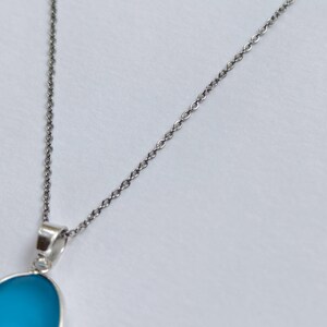 Pu&ograve; includere: Una collana d'argento con un pendente. Il pendente ha una pietra blu chiaro a forma ovale. La catena &egrave; delicata e il pendente &egrave; incastonato in una lunetta d'argento. La collana &egrave; mostrata su sfondo bianco.