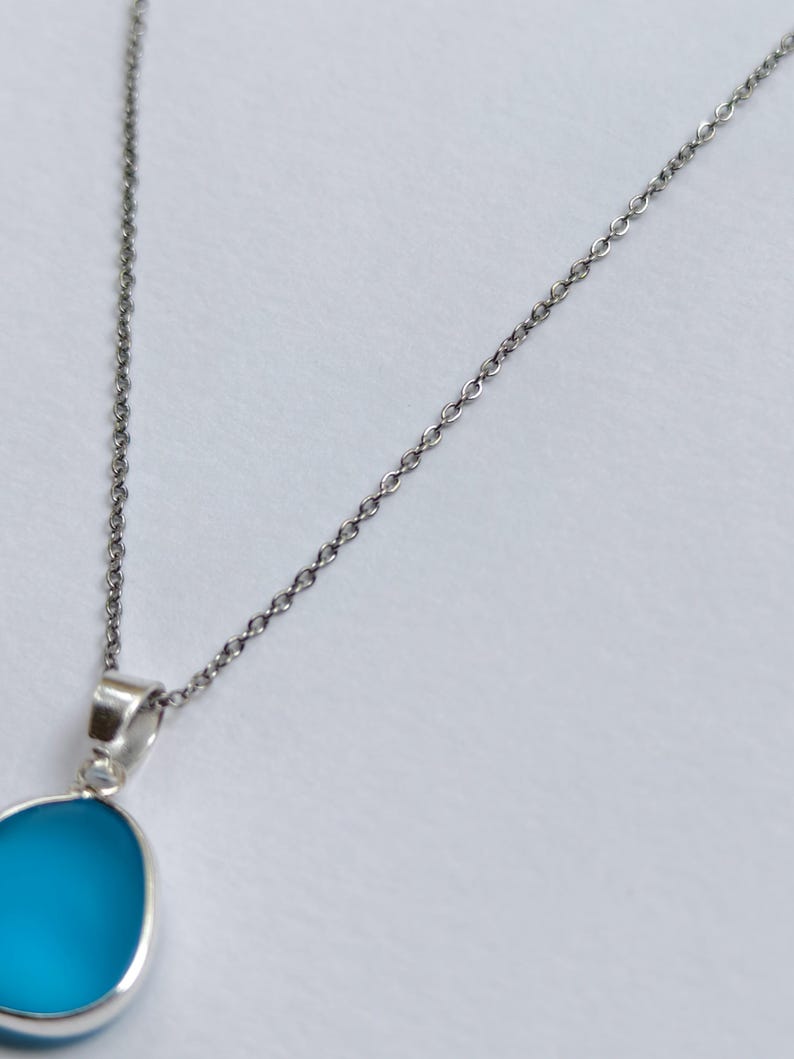 Pu&ograve; includere: Una collana d'argento con un pendente. Il pendente ha una pietra blu chiaro a forma ovale. La catena &egrave; delicata e il pendente &egrave; incastonato in una lunetta d'argento. La collana &egrave; mostrata su sfondo bianco.