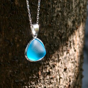 Pu&ograve; includere: Una collana d'argento con un ciondolo triangolare azzurro. Il ciondolo ha un aspetto liscio e smerigliato, incastonato in una lunetta d'argento. La catena &egrave; delicata, appesa su uno sfondo sfocato e strutturato.