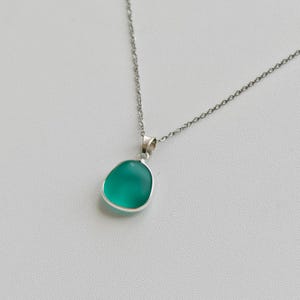 Pu&ograve; includere: Una collana d'argento con un pendente. Il pendente ha una pietra liscia, arrotondata, color verde acqua incastonata in una lunetta d'argento. Pende da una delicata catena d'argento. Il pendente ha una finitura lucida.