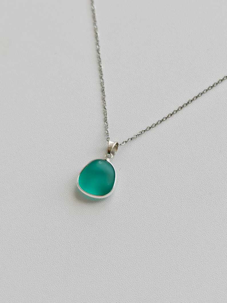 Pu&ograve; includere: Una collana d'argento con un pendente. Il pendente ha una pietra liscia, arrotondata, color verde acqua incastonata in una lunetta d'argento. Pende da una delicata catena d'argento. Il pendente ha una finitura lucida.