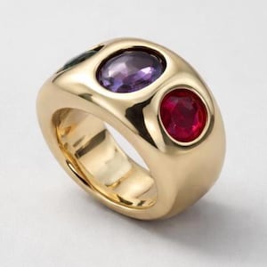 Peut inclure: Une bague large en or poli avec trois pierres précieuses rondes serties à fleur. Les pierres comprennent une améthyste violette profonde, un rubis rouge vif et une émeraude vert foncé, incrustées dans la surface métallique lisse et arrondie.