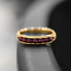 May include: A gold band ring with a row of small, dark red gemstones.
