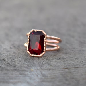 Peut inclure: Une bague en or rose avec une pierre précieuse rouge foncé de taille émeraude. La bague a une double bande.