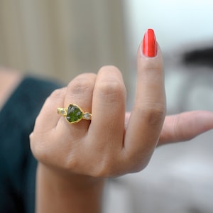May include: A gold ring featuring a green gemstone and smaller white gemstones set into the band.