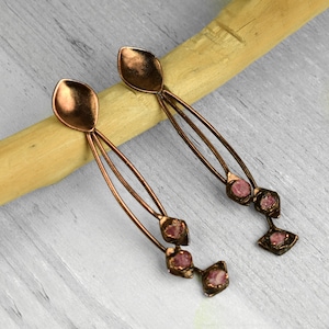 May include: A pair of long, copper earrings with three pink gemstone accents on each earring.