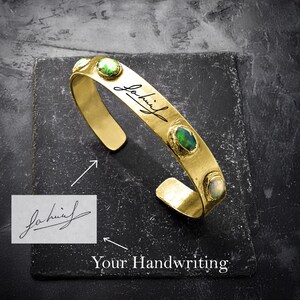 Pode incluir: Pulseira de bracelete de ouro com pedras preciosas verdes e brancas e uma inscrição manuscrita que diz "John" sobre um fundo preto.