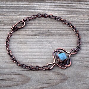 Puede incluir: Un brazalete de cadena de cobre con una piedra preciosa azul engastada en un diseño de alambre de cobre.