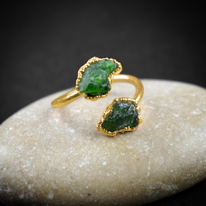 May include: A gold ring with two green gemstone settings. The ring is open and adjustable.