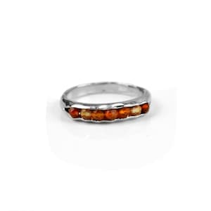 May include: A silver band ring with a row of orange and brown gemstones.