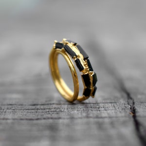 May include: A gold ring with black rectangular stones set in a geometric pattern.