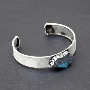 May include: A silver cuff bracelet with a large, dark blue, irregularly shaped gemstone set into the metal.