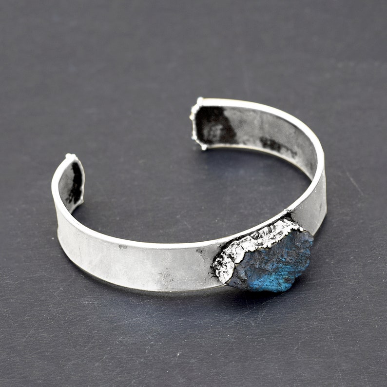 May include: A silver cuff bracelet with a large, dark blue, irregularly shaped gemstone set into the metal.