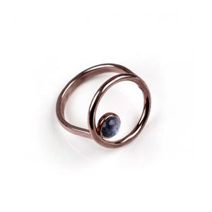 Puede incluir: Un anillo de oro rosa con una sola piedra preciosa azul engastada en un dise&ntilde;o circular.