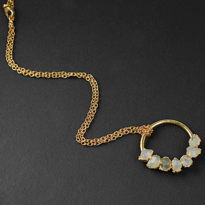 Puede incluir: Un collar de cadena dorada con un colgante circular que presenta una fila de piedras facetadas transparentes.