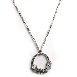 Puede incluir: Un collar de cadena de plata con un colgante circular que presenta un grupo de diamantes grises en bruto.