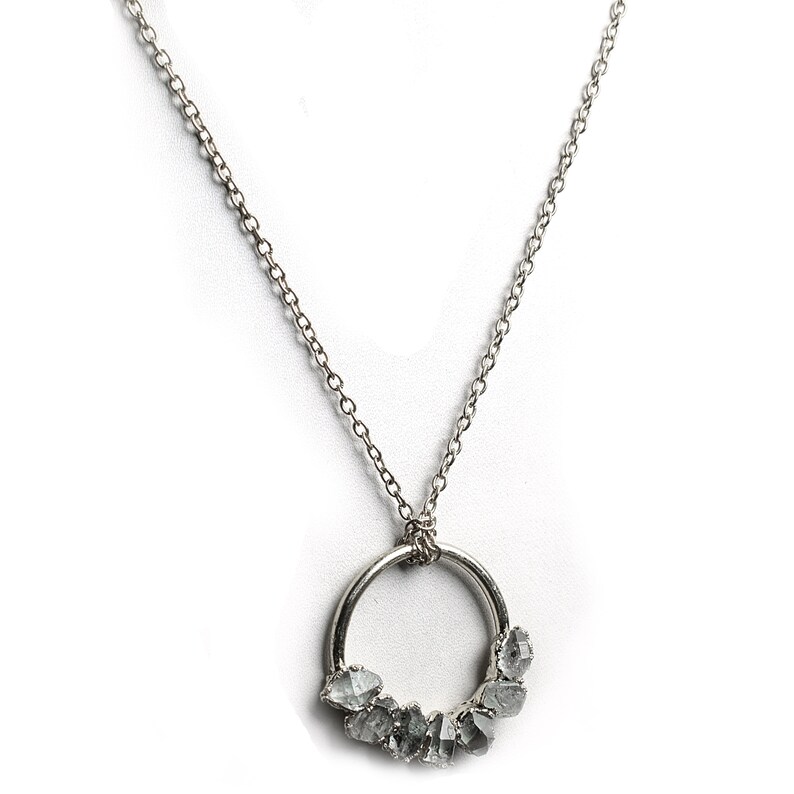 Puede incluir: Un collar de cadena de plata con un colgante circular que presenta un grupo de diamantes grises en bruto.