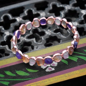 May include: A copper wire bracelet with a row of faceted gemstones in shades of purple, white, and orange.