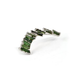 Puede incluir: Un pendiente de plata con un dise&ntilde;o curvo adornado con m&uacute;ltiples piedras preciosas verdes.