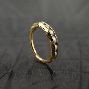 Pode incluir: Um anel de ouro com uma fileira de pequenas pérolas brancas engastadas na banda.