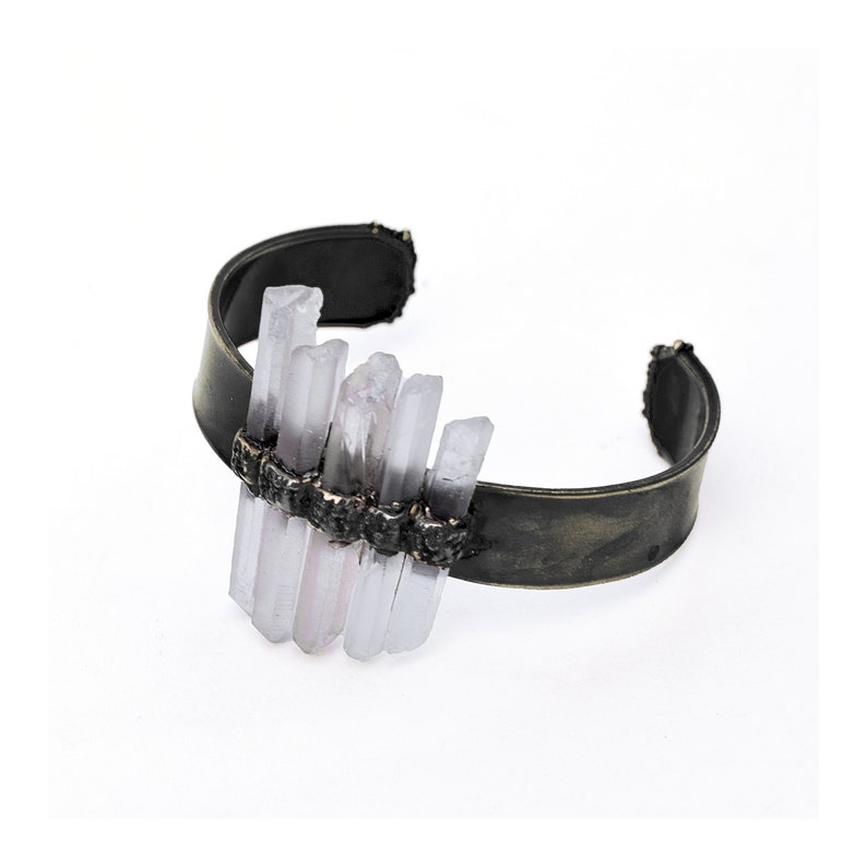 May include: A silver cuff bracelet featuring a cluster of clear quartz crystals set into the metal. The crystals are arranged in a staggered pattern, creating a unique and eye-catching design.