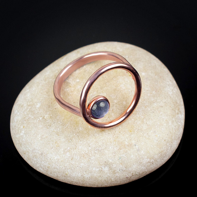 Puede incluir: Un anillo de oro rosa con un delicado dise&ntilde;o circular y una peque&ntilde;a piedra preciosa azul claro en el centro.