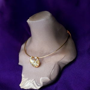 May include: A gold choker necklace with a decorative pendant featuring a stylized shell design with clear rhinestones. The necklace is displayed on a light brown mannequin bust.