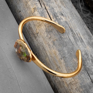 Puede incluir: Un brazalete de oro con una gran piedra de ópalo iridiscente engastada en la banda.