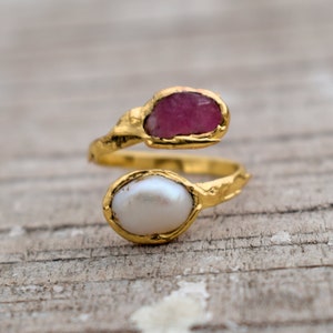 May include: A gold ring with a pink stone and a white pearl. The ring is twisted and has a textured finish.