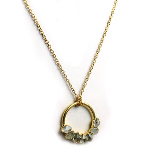 Puede incluir: Un collar de cadena dorada con un colgante circular que presenta un grupo de peque&ntilde;as piedras preciosas grises sin pulir.