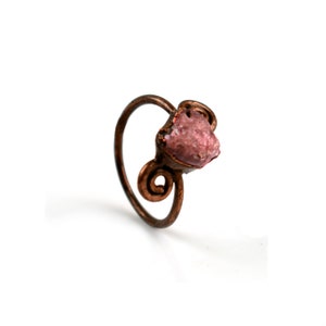 Può includere: Un anello in rame con una pietra preziosa grezza rosa incastonata in un design a filo ritorto.