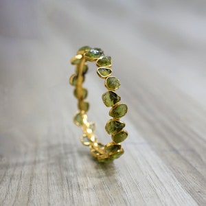 May include: A gold bangle bracelet with a row of green gemstone beads. The beads are irregular in shape and have a rough, natural texture.