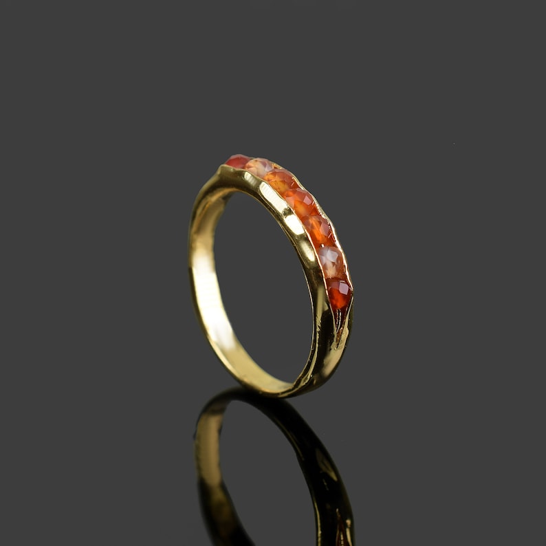 May include: A gold ring with a row of orange carnelian gemstones set into the band.