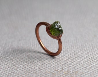 May include: A copper ring with a raw green gemstone set in the band.