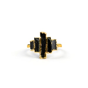 Könnte beinhalten: Ein goldener Ring mit einem schwarzen Stein in der Mitte. Der Stein besteht aus mehreren schwarzen Steinen, die vertikal angeordnet sind.