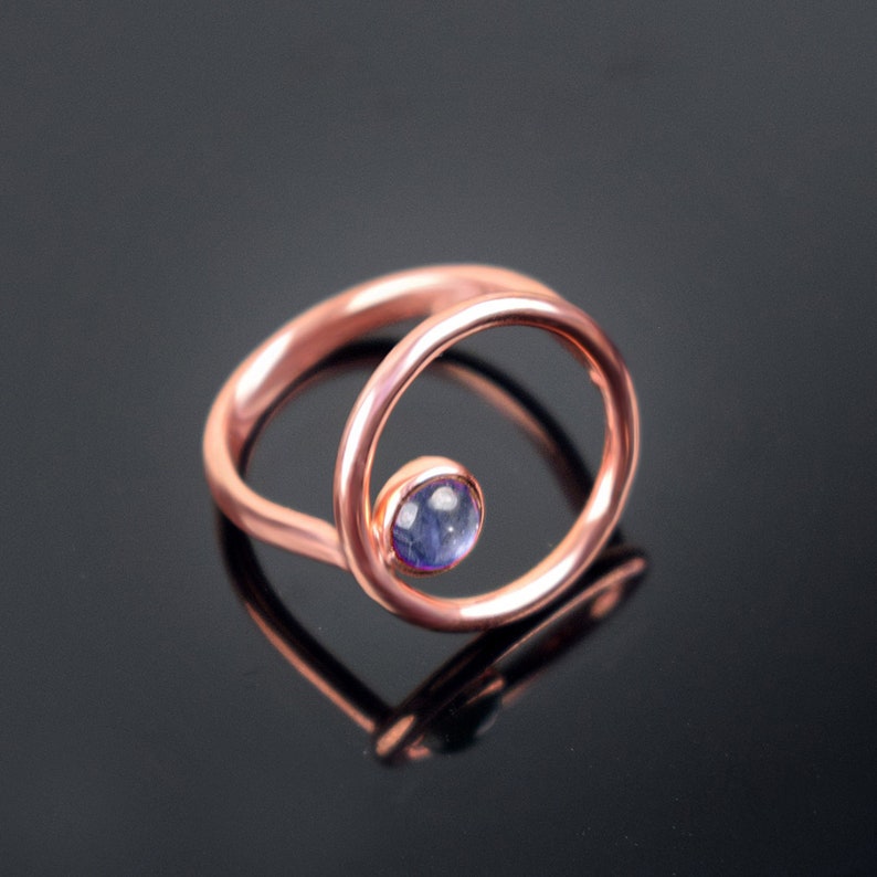 Puede incluir: Un anillo de cobre con una piedra preciosa azul engastada en un dise&ntilde;o circular.