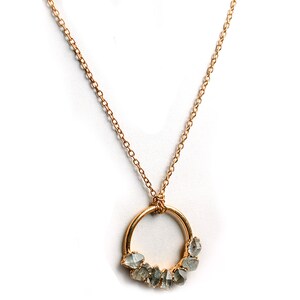 Puede incluir: Un collar de cadena dorada con un colgante circular que presenta un grupo de piedras preciosas sin pulir de color gris claro.