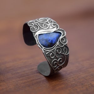 May include: A silver cuff bracelet with a blue gemstone set in a swirl design.