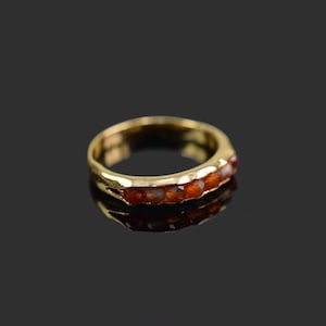 May include: A gold band ring with a row of six orange gemstones.
