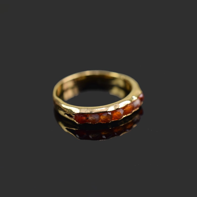 May include: A gold band ring with a row of six orange gemstones.