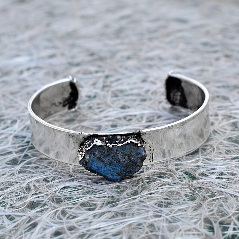 May include: A silver cuff bracelet with a large, blue, irregularly shaped gemstone set into the band.