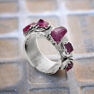 Pode incluir: Um anel de prata com uma banda decorada com um design floral e cravejada com cinco pedras preciosas cor-de-rosa.